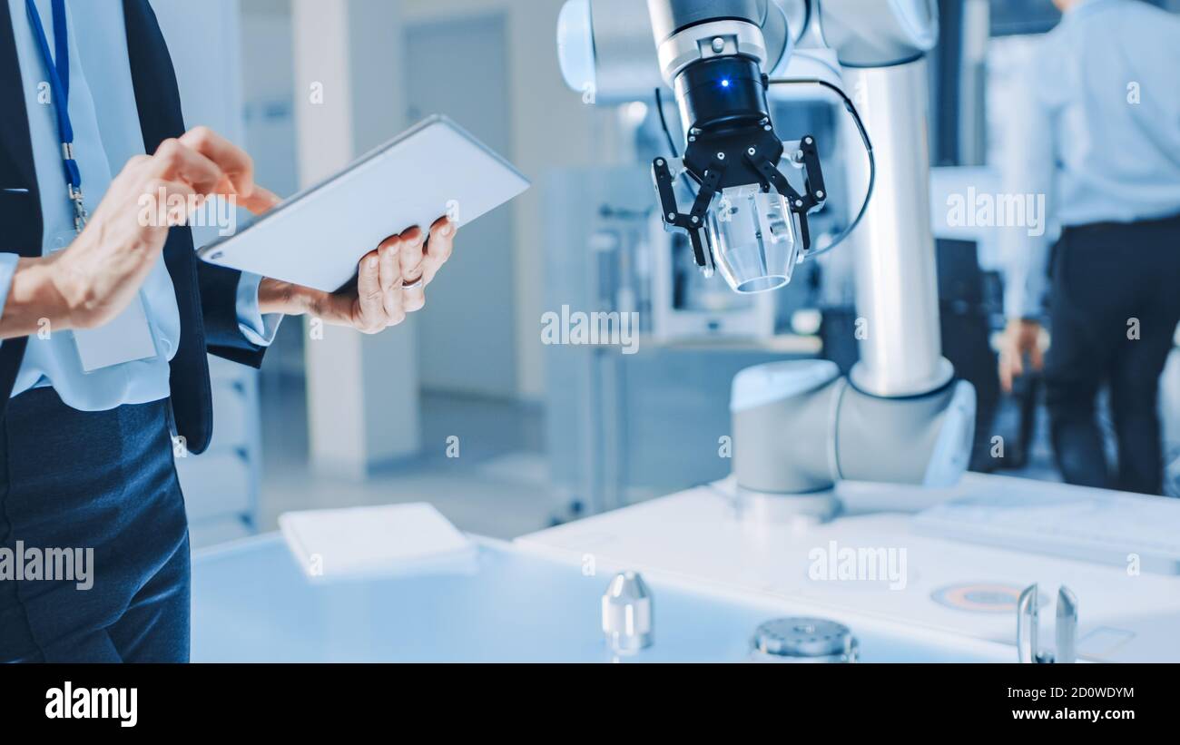 L'ingénieure en robotique industrielle féminine utilise une tablette pour programmer et manipuler le bras du robot pour le levage et le déplacement d'objets. Recherche technologique Banque D'Images