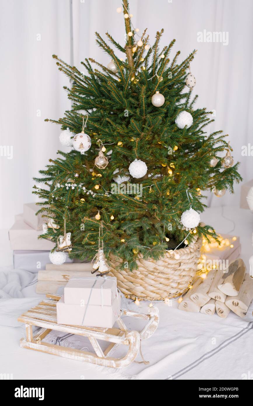 Arbre décoré de Noël dans un pot en osier décoré de jouets blancs. À côté de l'arbre il y a des luges décoratives en bois avec des cadeaux Banque D'Images