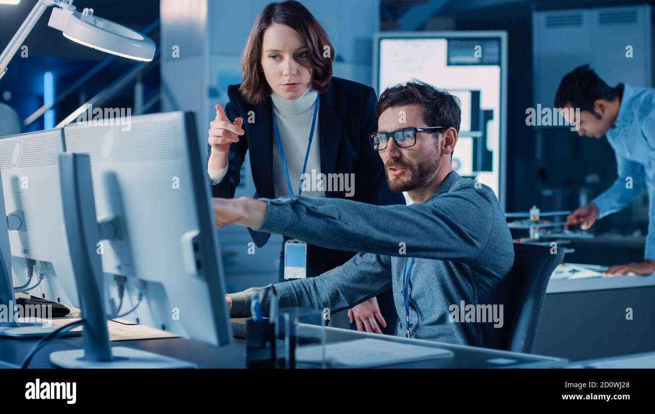 Un ingénieur futuriste de développement de machines-moteurs travaillant sur l'ordinateur à son bureau, s'entretient avec une femme responsable de projet. Équipe de professionnels travaillant dans Banque D'Images