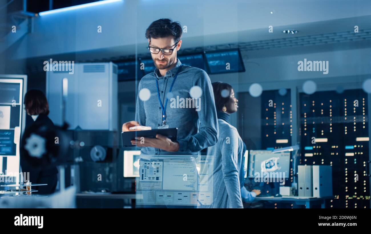 Dans l'installation de recherche technologique : l'ingénieur en chef est au milieu du laboratoire et utilise un Tablet PC. Équipe d'ingénieurs industriels, développeurs Banque D'Images
