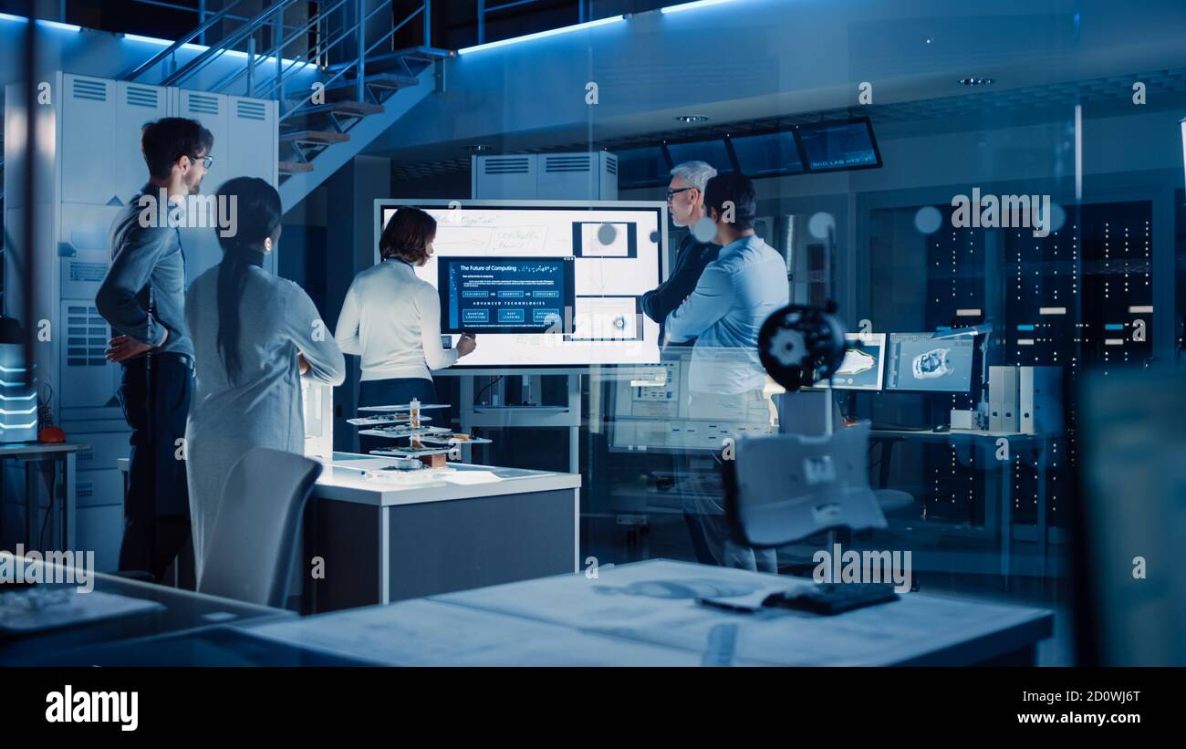 Réunion des ingénieurs dans le laboratoire de recherche technologique : une femme dirige une présentation à l'aide d'un tableau blanc numérique vertical, montre un modèle de machine Banque D'Images