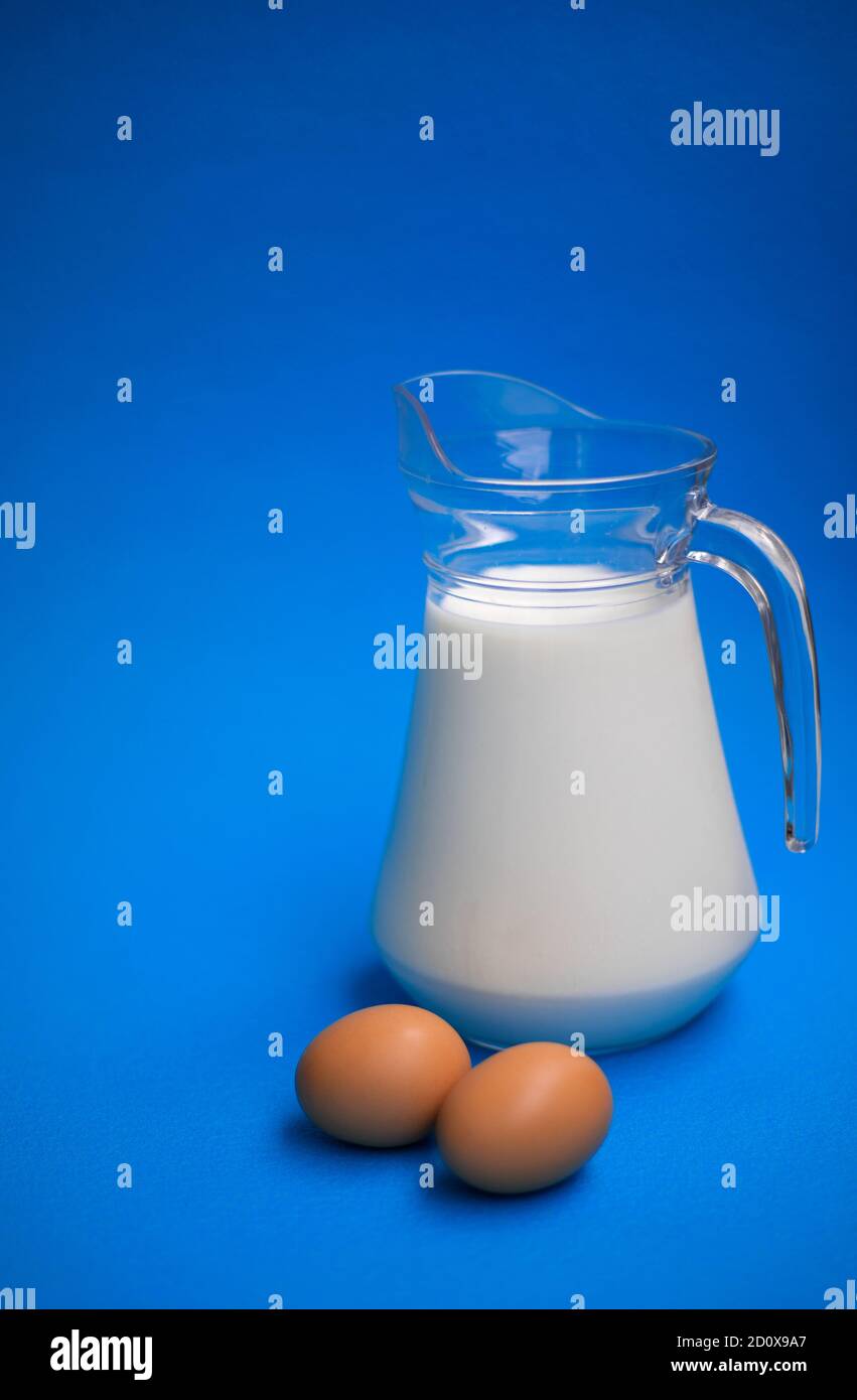 Lait dans un pot en verre et deux œufs sur un arrière-plan bleu Banque D'Images