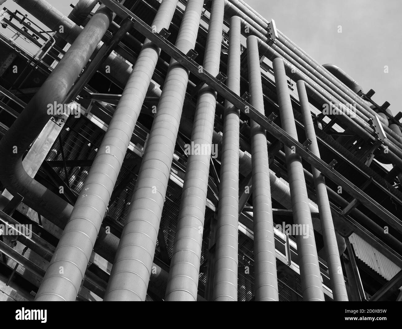 Vue en noir et blanc de l'ancienne tour de raffinerie de pétrole et de pétrochimie recouverte de tuyaux industriels rouillés. Banque D'Images