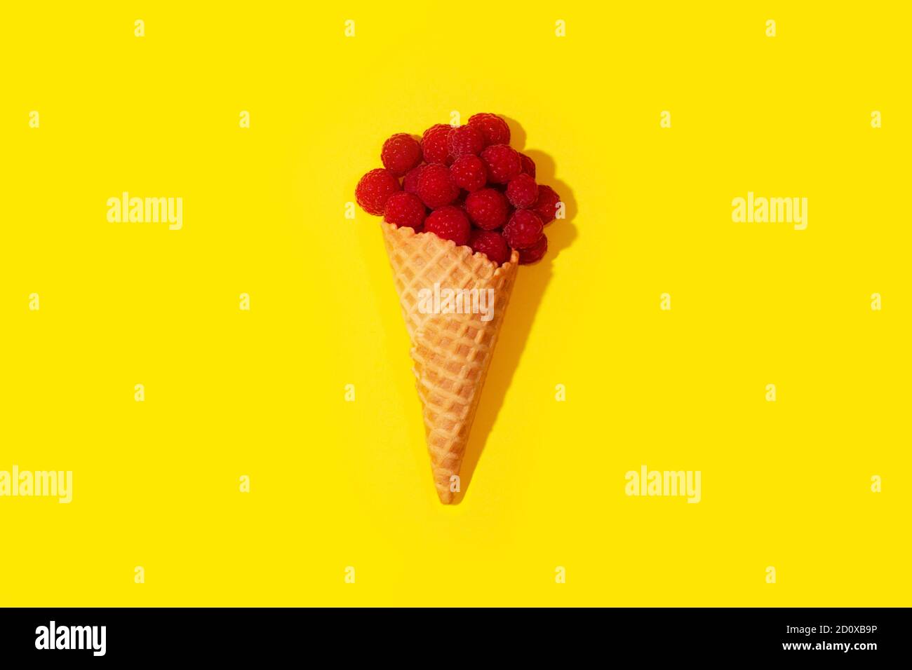 L'art conceptuel des framboises dans un cornet de crème glacée sur une table, sur un fond jaune. Peu de surréalisme. Banque D'Images