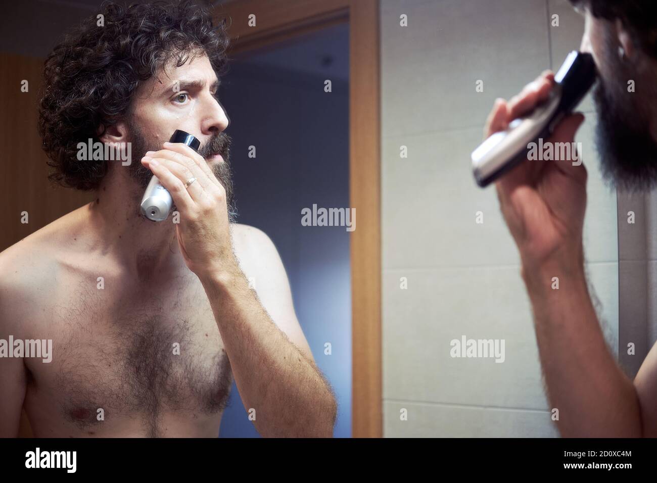 Homme hispanique d'âge moyen coupant sa barbe Banque D'Images