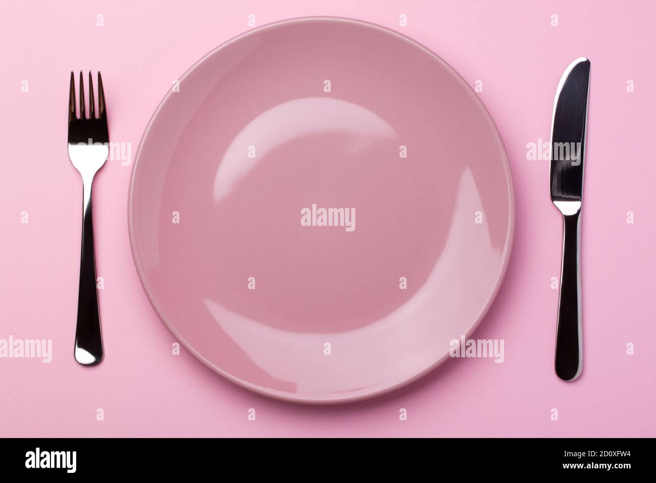 Assiette rose brillante avec couverts en métal - fourchette et couteau sur fond de papier rose. Banque D'Images