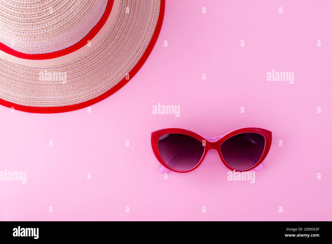 Lunettes de soleil rouges et chapeau de plage brillant sur fond rose clair. Banque D'Images