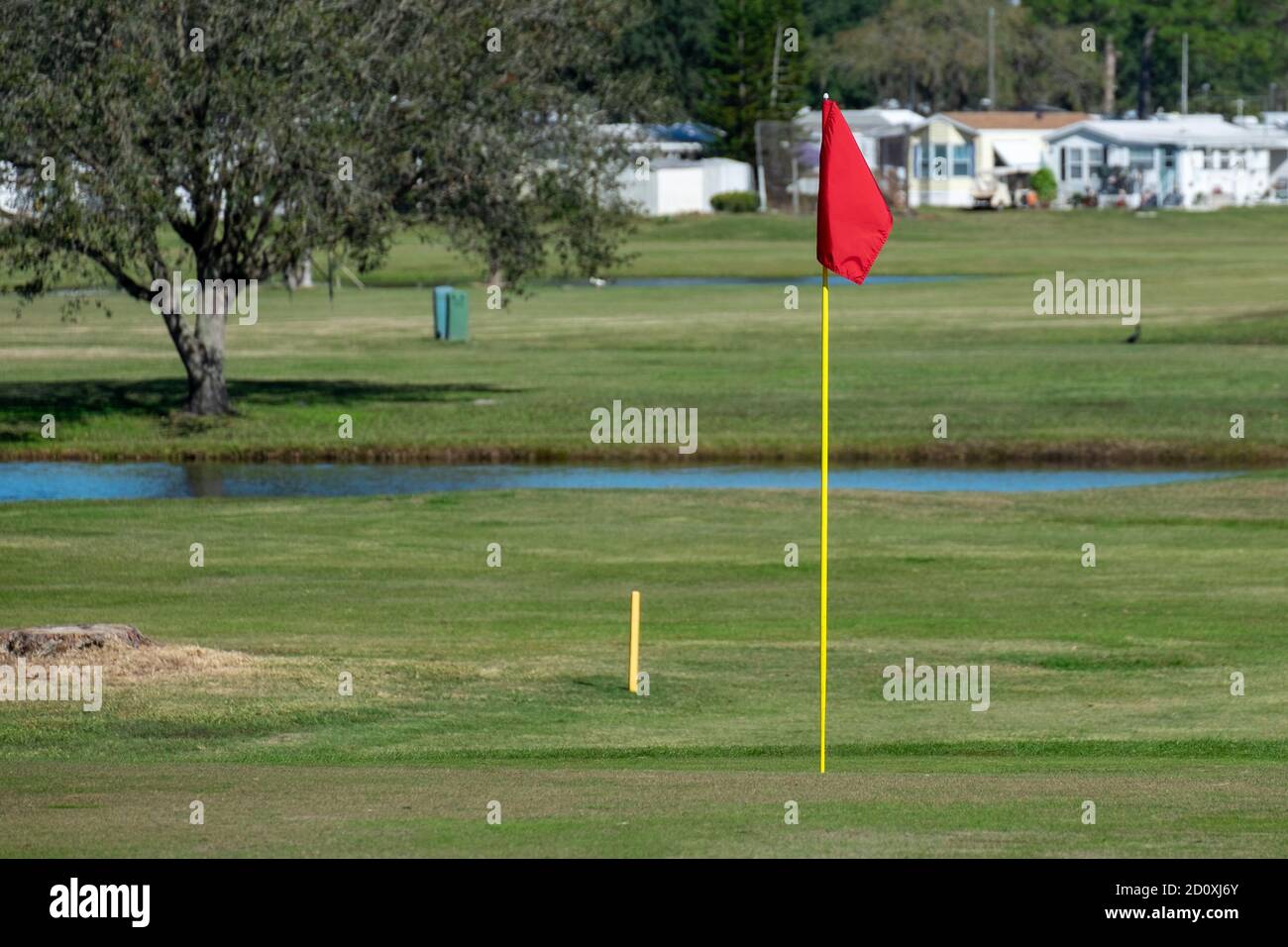 Un drapeau rouge se dresse sans mouvement attaché à un poteau jaune, à un trou de golf, sur un terrain de golf. Il y a des remorques de véhicules de camping en arrière-plan. Banque D'Images