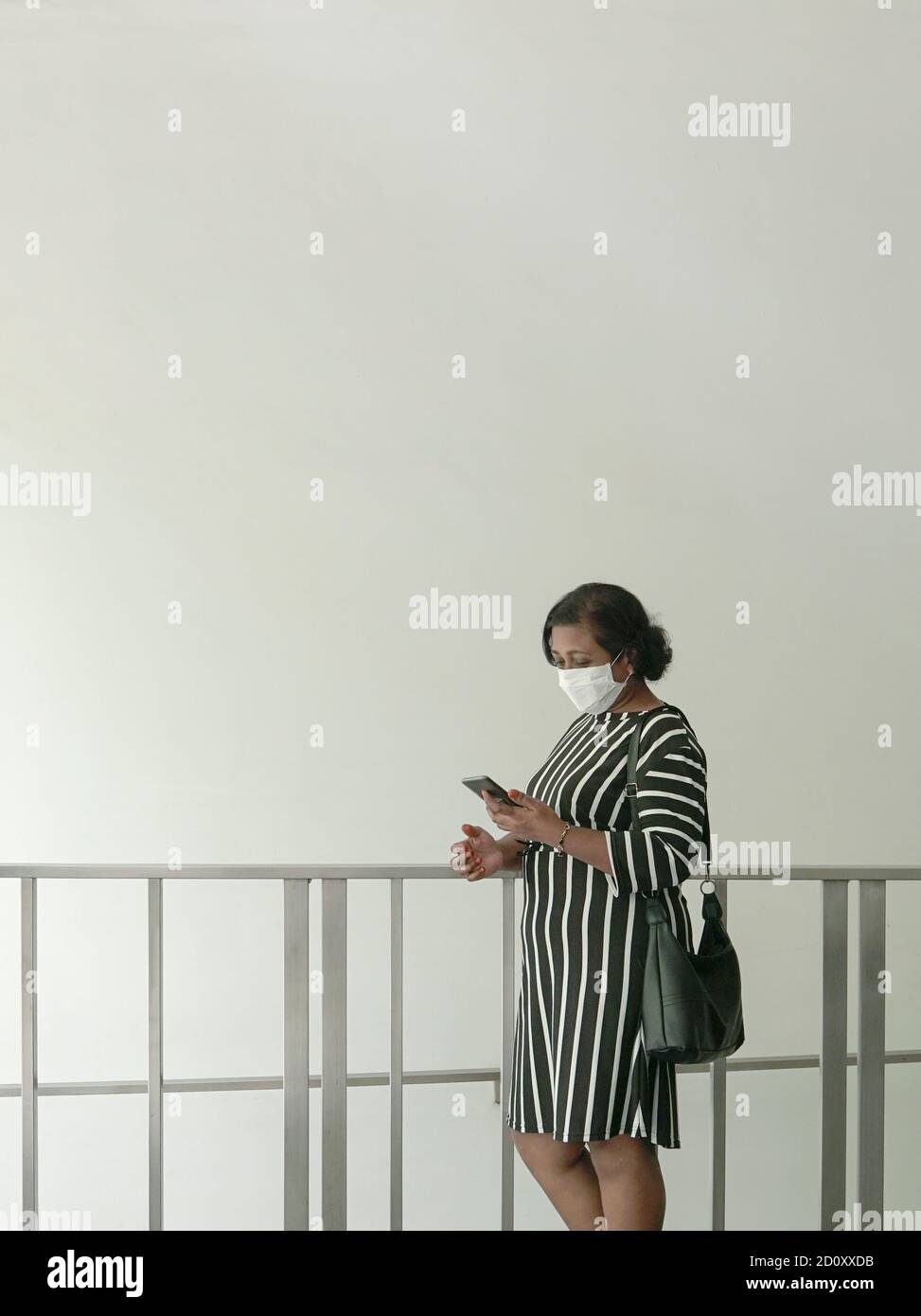 Femme avec un sac à main et portant un masque facial lisant son téléphone portable. Copier l'espace. Banque D'Images