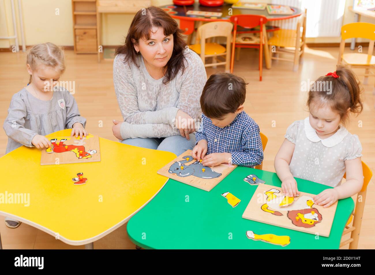 Le professeur d'enfants d'âge préscolaire avec trois élèves collectent le puzzle Banque D'Images