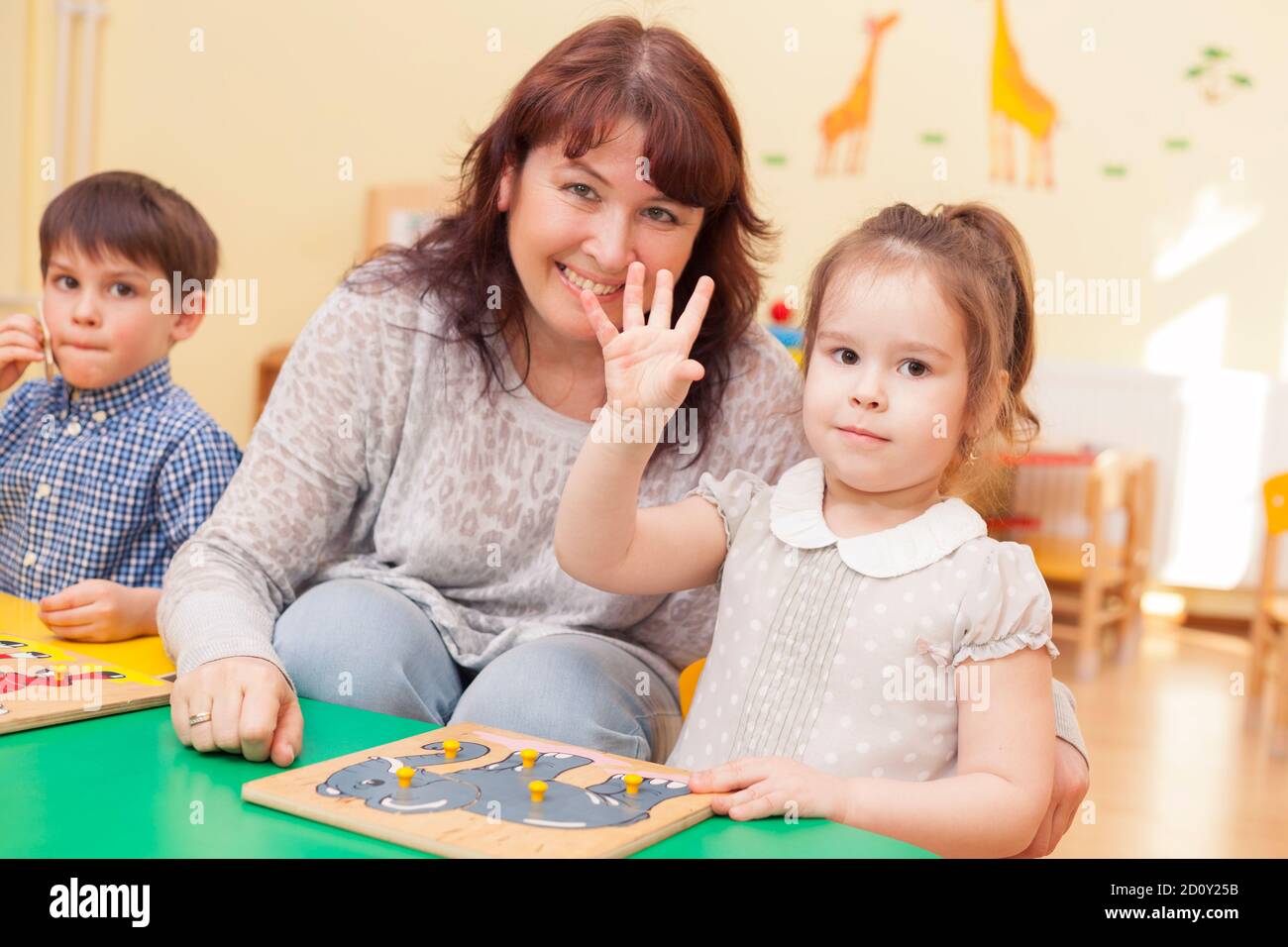 une petite fille mignonne a soulevé la main pour répondre. enseignante assise à côté. Belle femme caucasienne mature. Ils regardent la caméra et sourient. Horiz Banque D'Images
