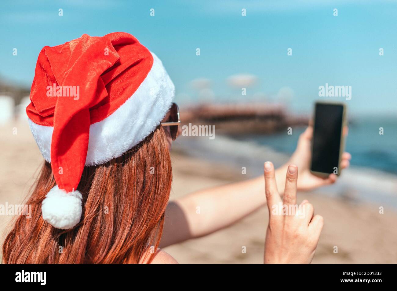 Jeune belle fille dans un chapeau rouge du père noël et maillot de bain fait un selfie sur le bord de mer Banque D'Images