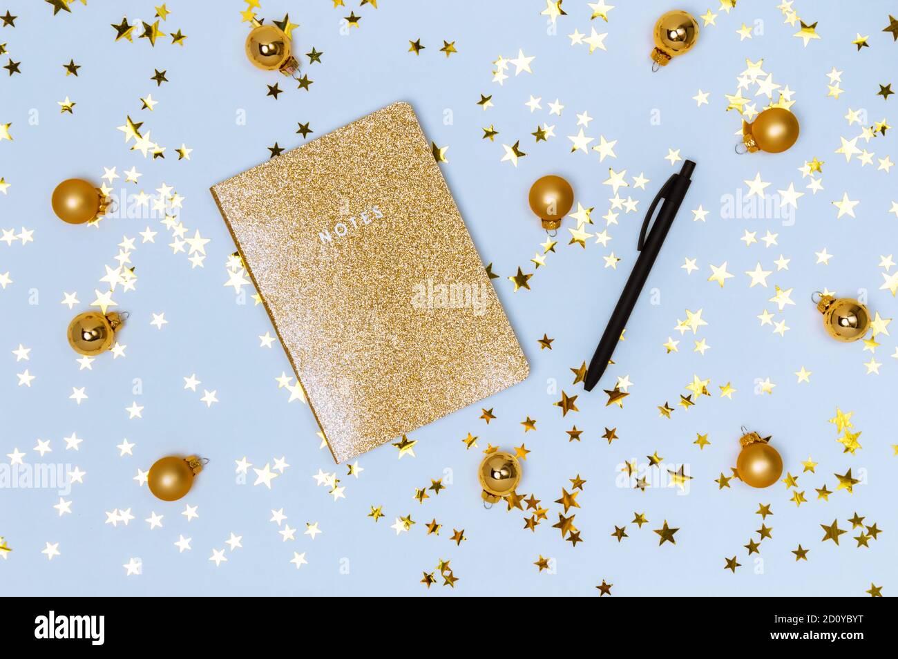 Carnet doré avec couverture scintillante brillante, stylo noir et boules de Noël dorées, boules et confettis étoiles sur fond bleu. Liste de souhaits, nouvel an reso Banque D'Images