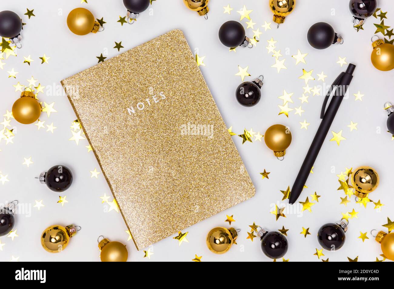 Carnet doré avec couverture scintillante, boules de Noël dorées et noires, boules et étoiles confettis. Bilan de l'année, liste de souhaits, résolutions du nouvel an Banque D'Images