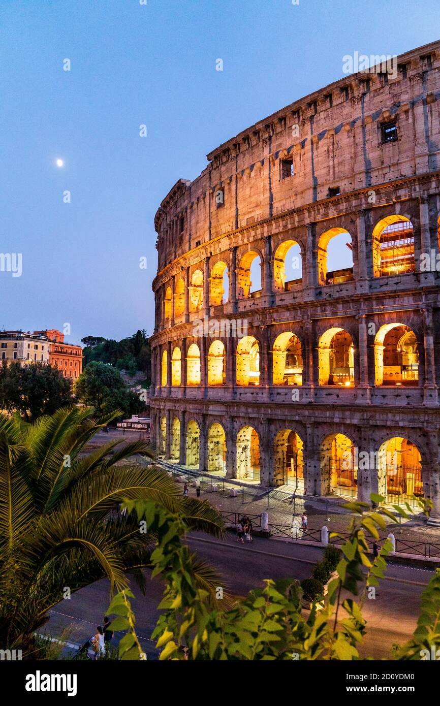 Section du Colisée romain illuminé de rome pendant l'heure bleue en début de soirée avec la lune se coucher dans un ciel clair. Banque D'Images