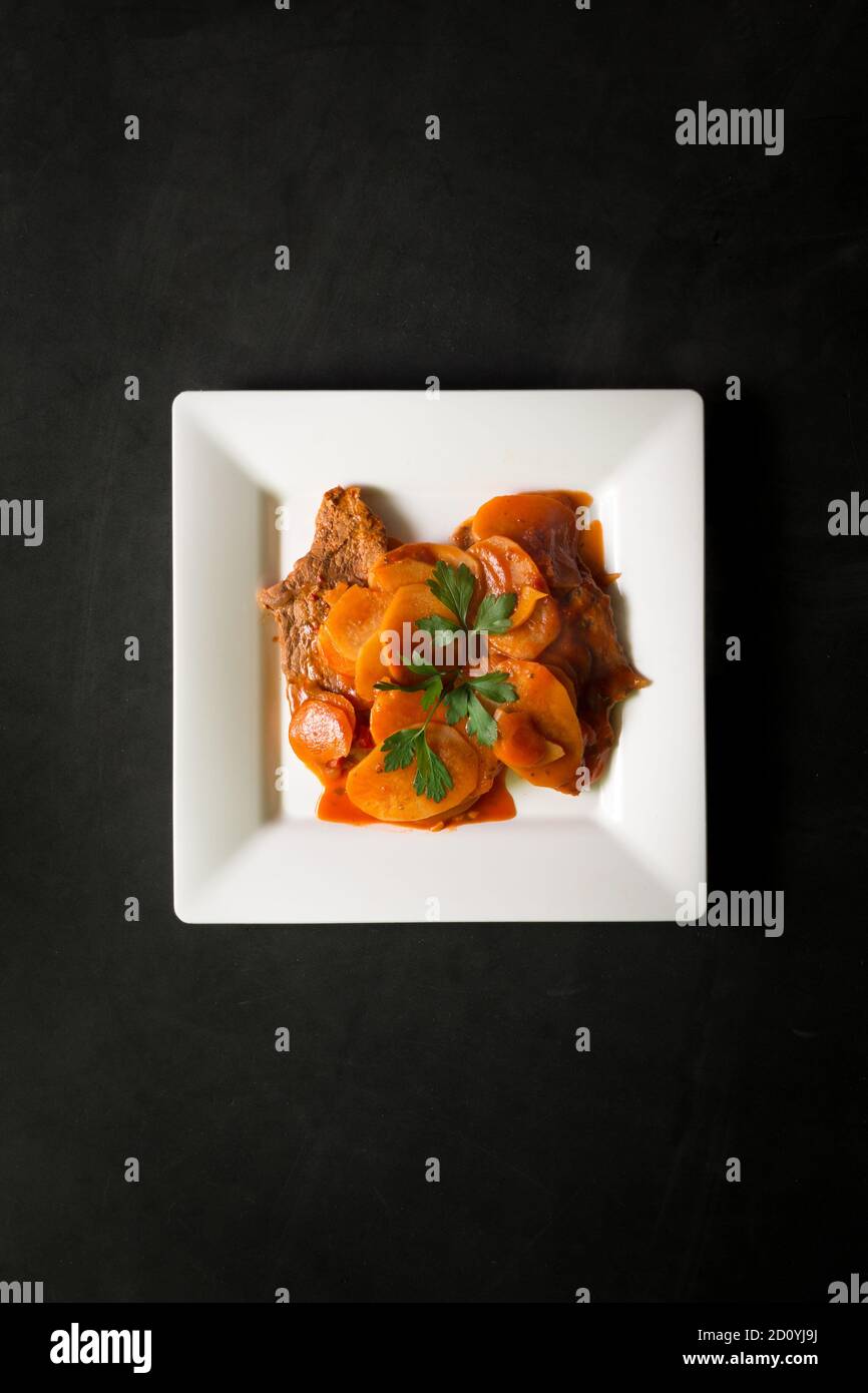 Steak avec carottes et pommes de terre sur une assiette blanche carrée sur fond noir Banque D'Images