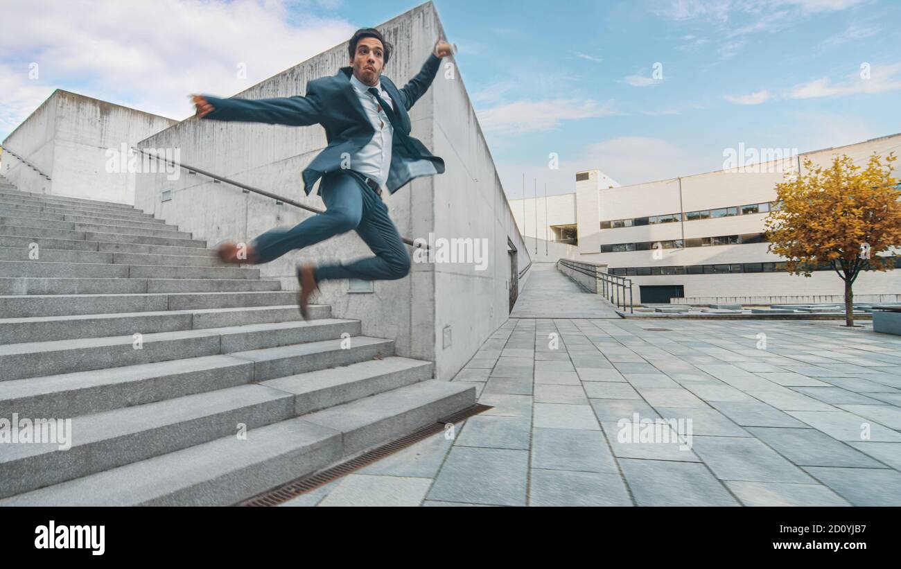 Joyeux et heureux homme d'affaires dans un costume tient le café et le saut en marchant sur les escaliers. Scène prise dans un parc en béton urbain à côté de Banque D'Images