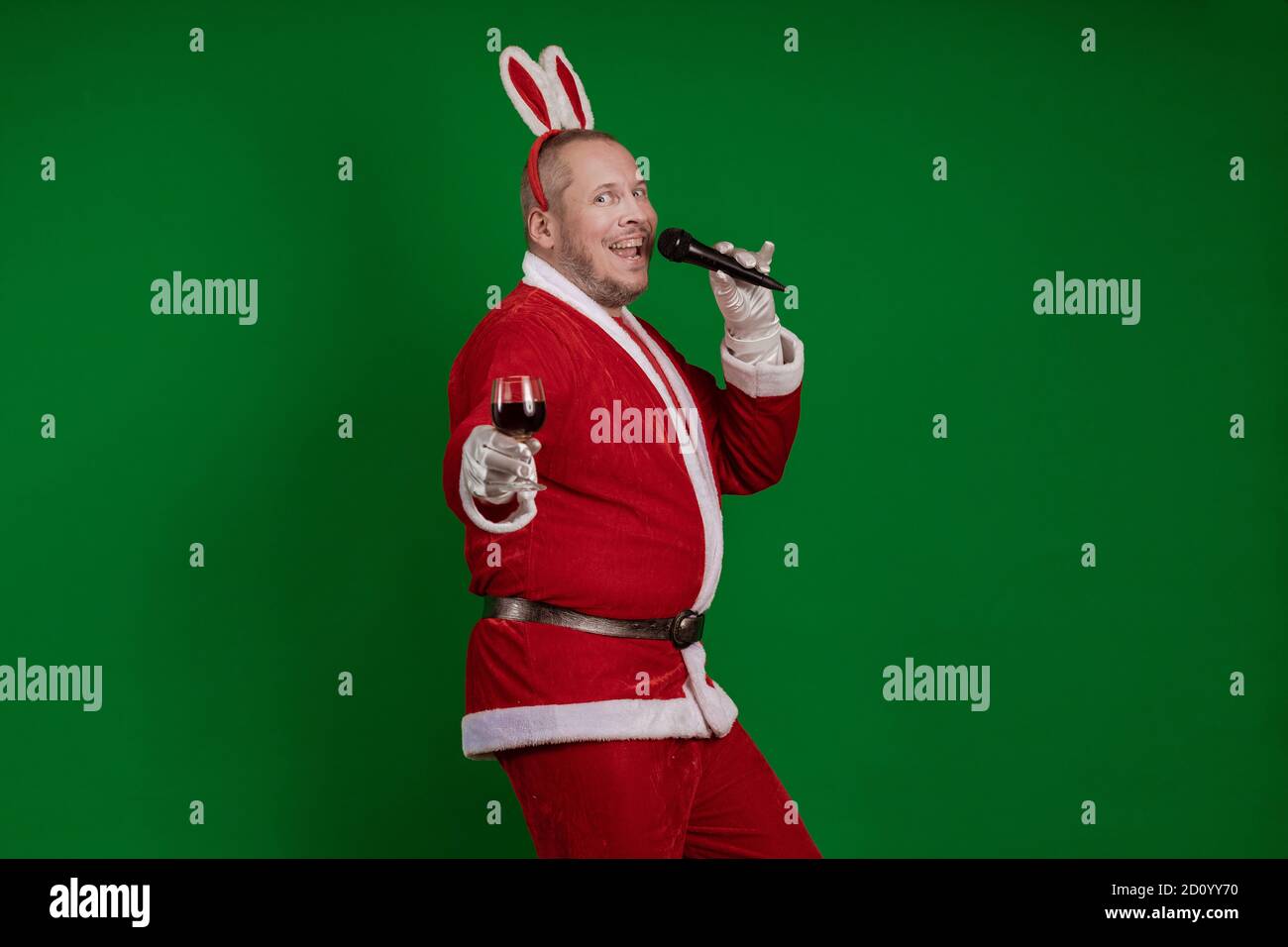 L'acteur émotionnel masculin dans un costume de Santa Claus tient un verre de vin entre ses mains et dit un toast au microphone et pose sur un chrome vert ca Banque D'Images