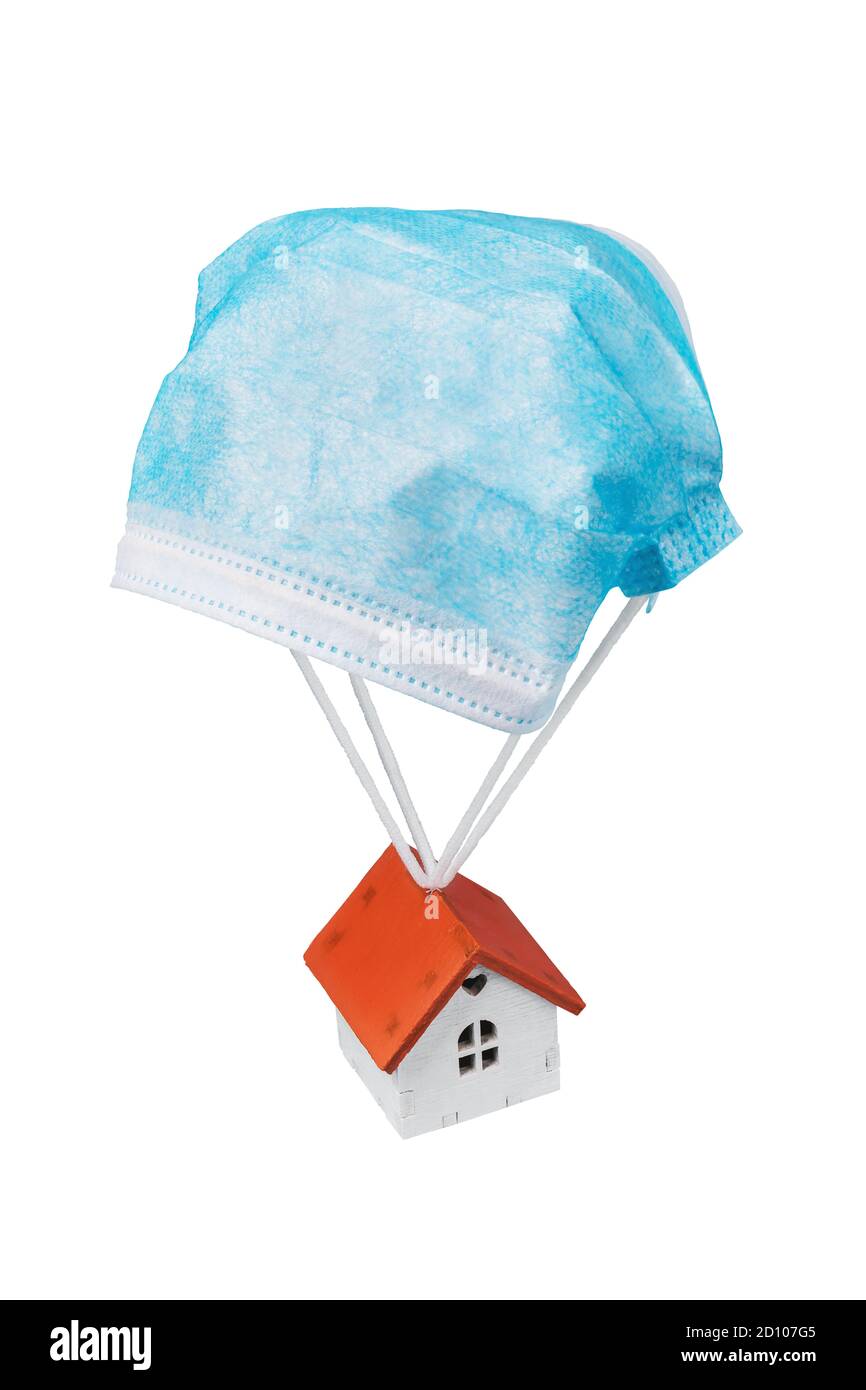 La maison de jouets vole sur un parachute à partir d'un masque médical isolé sur un fond blanc. Concept sur un lieu sûr pendant une pandémie Banque D'Images