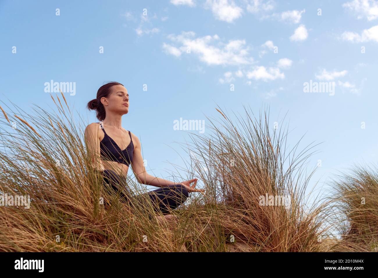 Femme mûre méditant sur la plage dans les dunes de sable avec un fond bleu ciel Banque D'Images