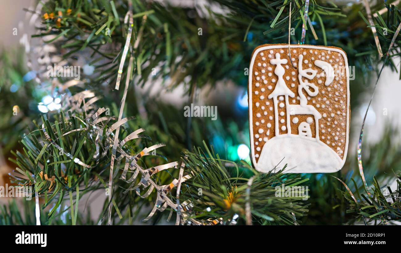 Pain d'épice sucré et corde argentée sur les aiguilles d'un arbre de Noël artificiel orné. Gros plan d'un biscuit traditionnel de Noël suspendu sur une branche verte. Banque D'Images