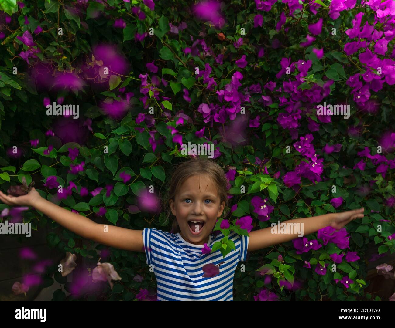 Portrait d'une petite fille gaie dans un magnifique fond floral. Un enfant heureux avec des mains levées, en profitant de la fraîcheur et de la beauté du jardin en fleurs. Banque D'Images