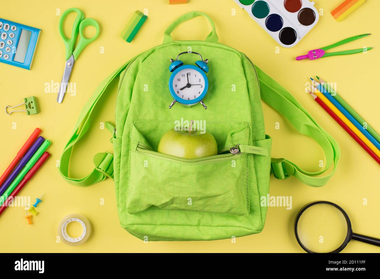 Se préparer pour le concept d'école. Haut au-dessus de la vue de la tête photo du réveil bleu pomme vert sac à dos coloré papeterie isolée sur le dos jaune Banque D'Images