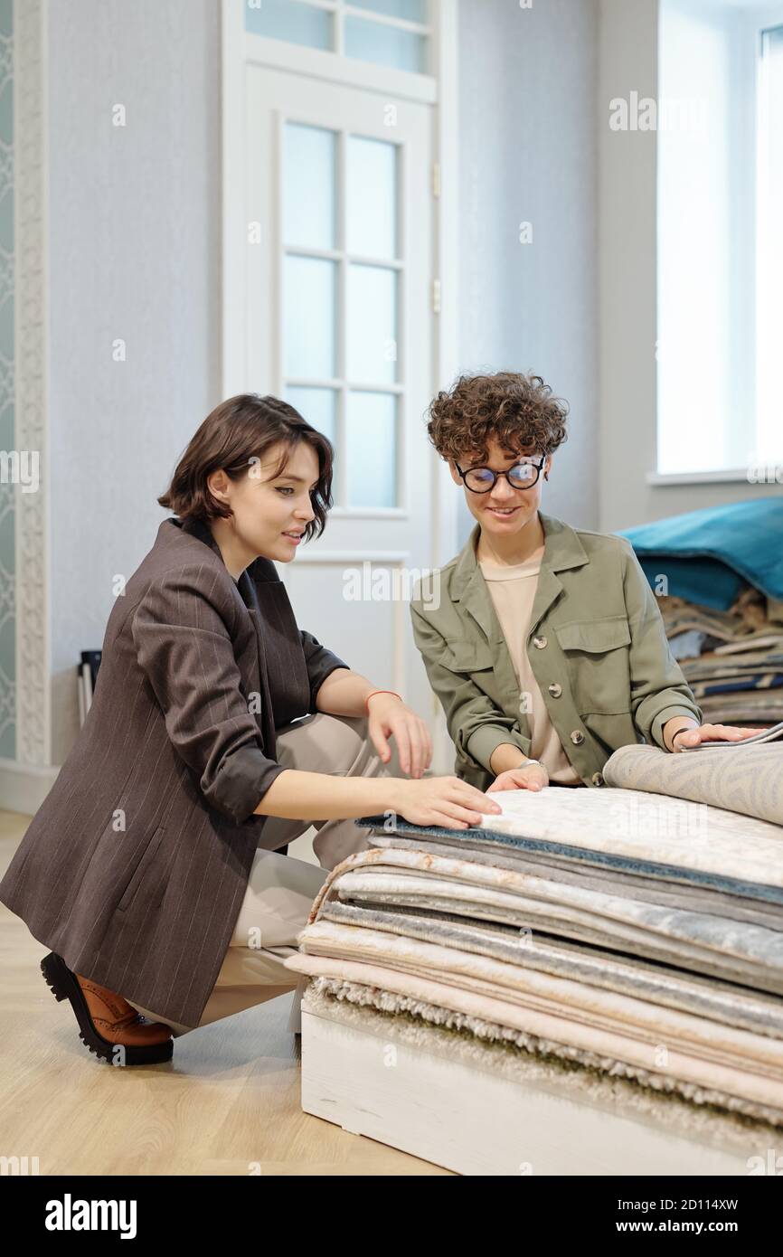 Jeune assistant d'atelier élégant aidant le client avec nouveau tapis ou revêtements de sol Banque D'Images
