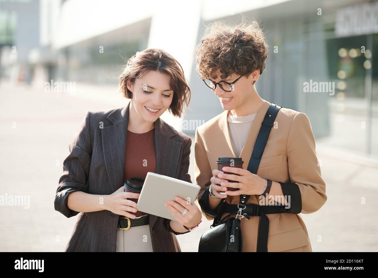 Deux jeunes collègues heureux avec des boissons regardant l'écran de tablette numérique Banque D'Images