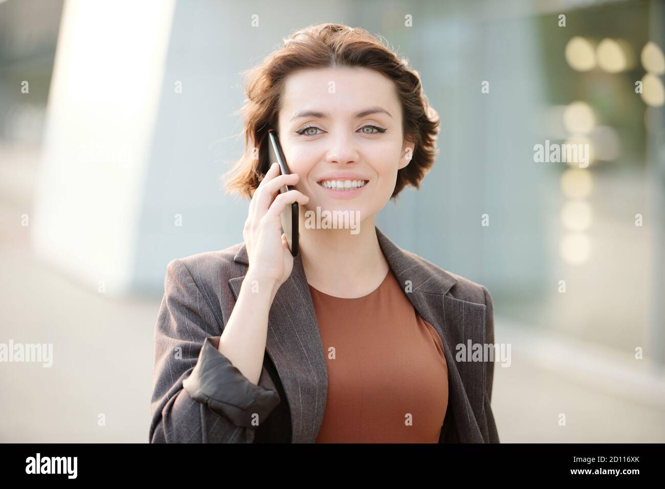 Jeune femme d'affaires souriante brune avec smartphone par client d'appel d'oreille Banque D'Images