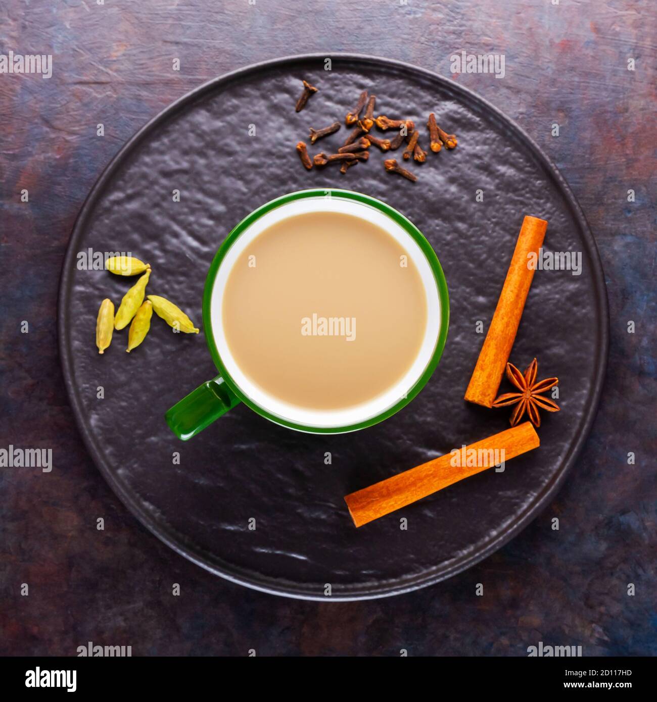 Thé Chai de masala. Boisson traditionnelle indienne - thé masala avec diverses épices sur une assiette noire. Tasse de thé aux épices en céramique sur fond sombre. Minimalis Banque D'Images