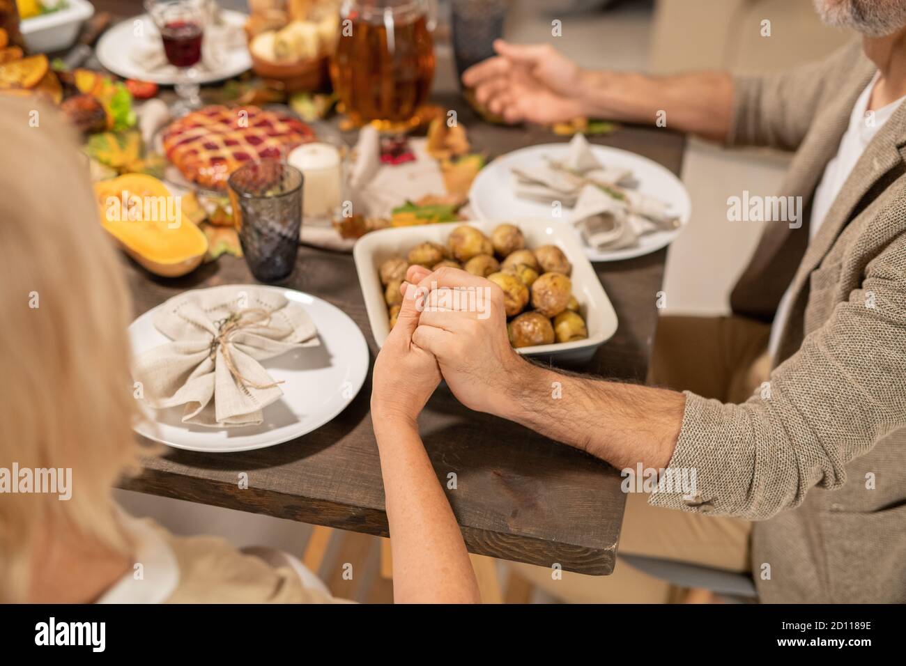 Mains de mari et de femme matures priant par table de fête servi pour le dîner Banque D'Images