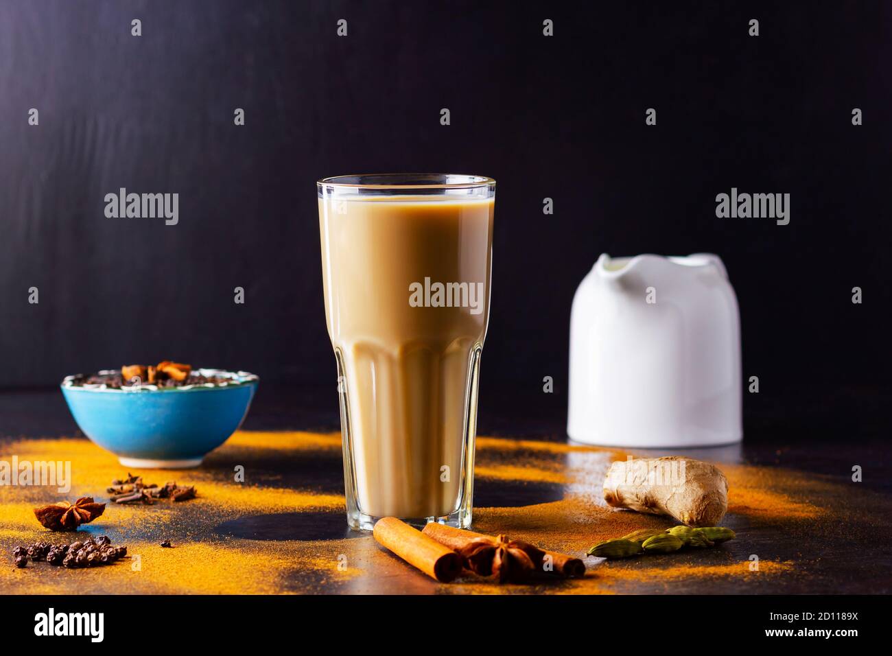 Verre de thé masala et épices éparses. Masala chai thé et pot à lait sur fond noir. Copier l'espace Banque D'Images