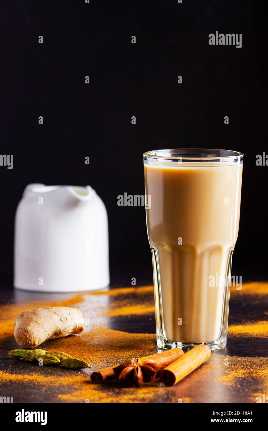 Verre de thé masala et épices éparses. Masala chai thé et pot à lait sur fond noir. Copier l'espace Banque D'Images