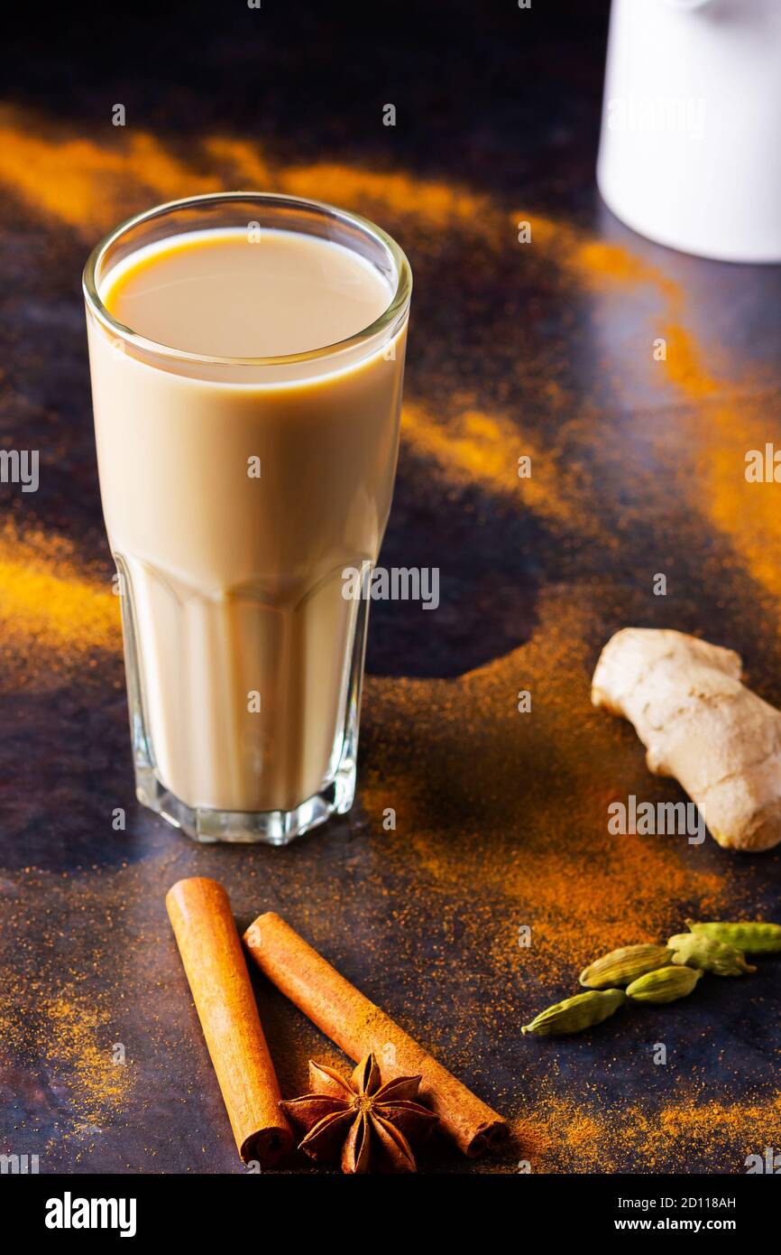 Verre de thé masala et épices éparses. Masala chai thé et pot à lait sur fond noir. Copier l'espace Banque D'Images