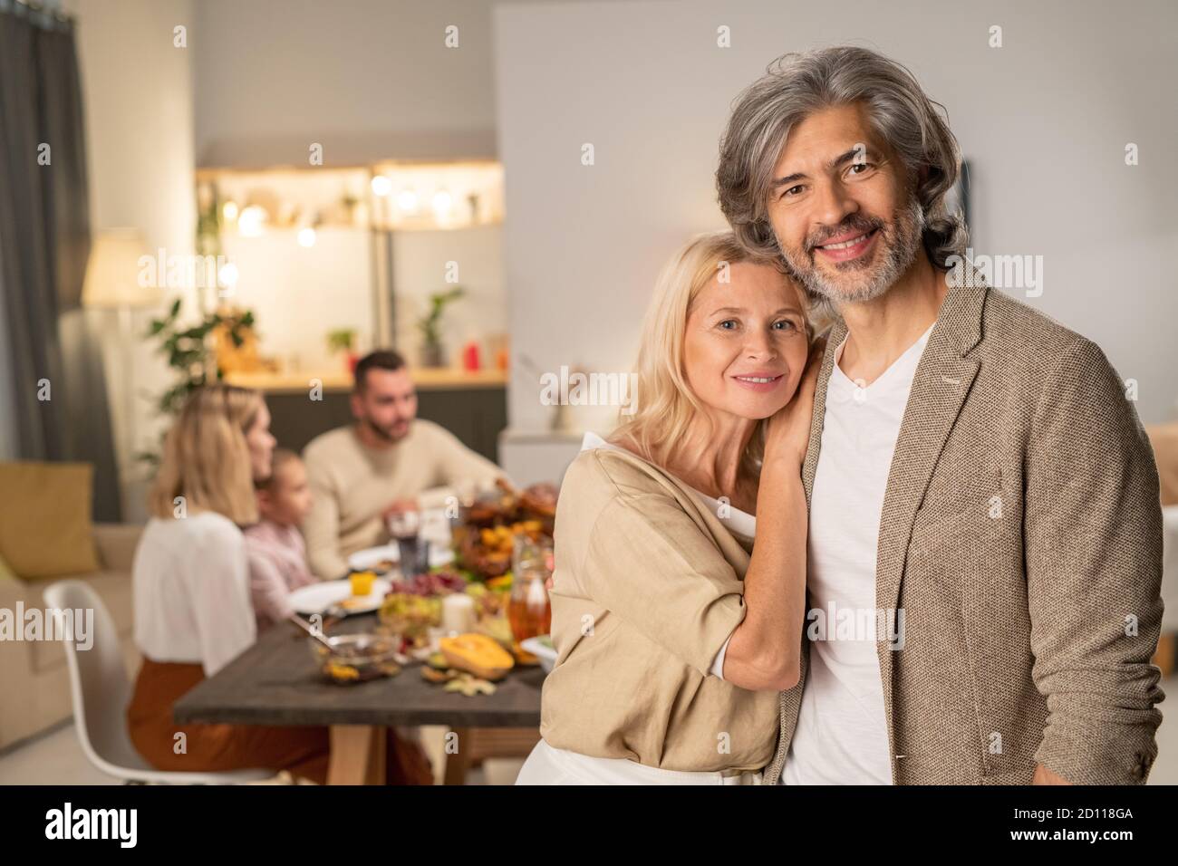 Couple d'âge mûr et gai debout devant l'appareil photo contre le dîner famille Banque D'Images