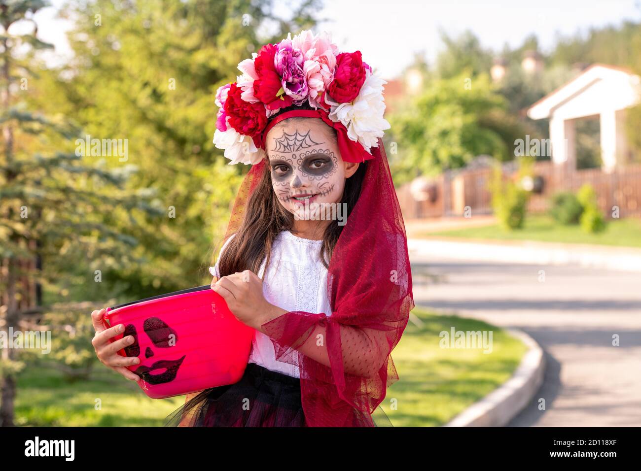 Petite fille souriante en costume de sorcière halloween tenant seau avec gâteries Banque D'Images