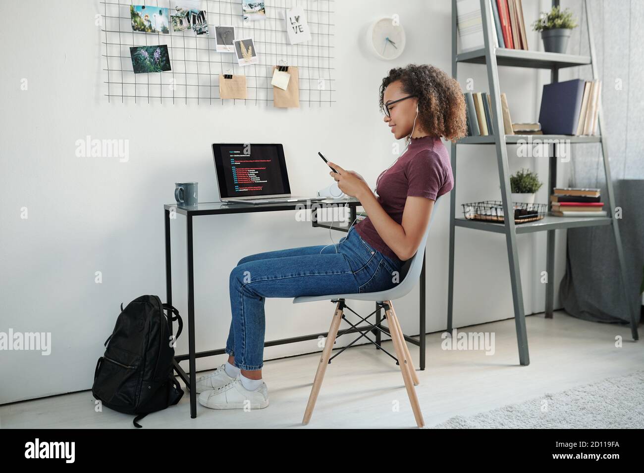 Jeune étudiante de race mixte joyeuse défilant dans un smartphone par ordinateur portable Banque D'Images
