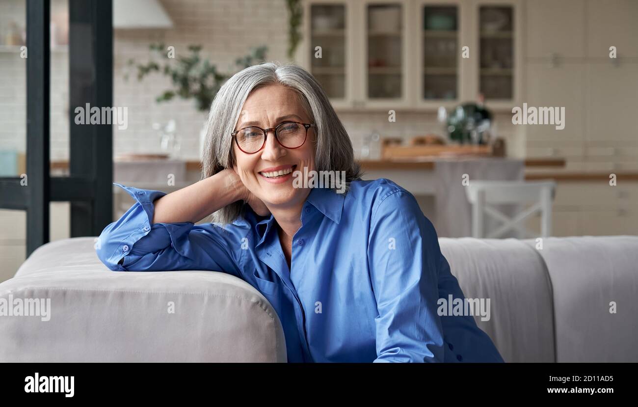 Heureuse détendue mature femme porte des lunettes assis sur le canapé à la maison, portrait. Banque D'Images