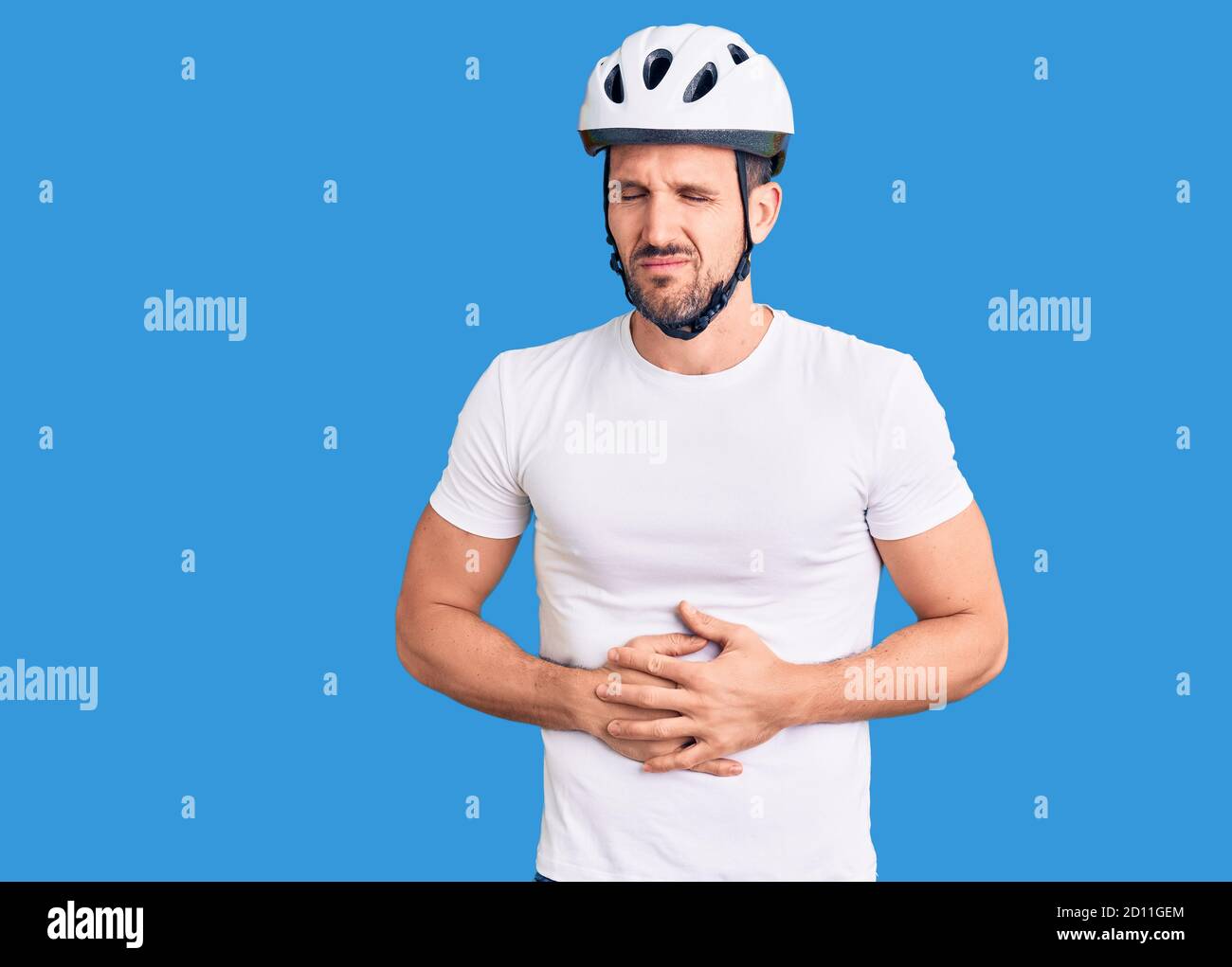 Jeune homme beau portant un casque de vélo avec la main sur l'estomac parce que l'indigestion, la maladie douloureuse sentiment malaise. Ache concept. Banque D'Images
