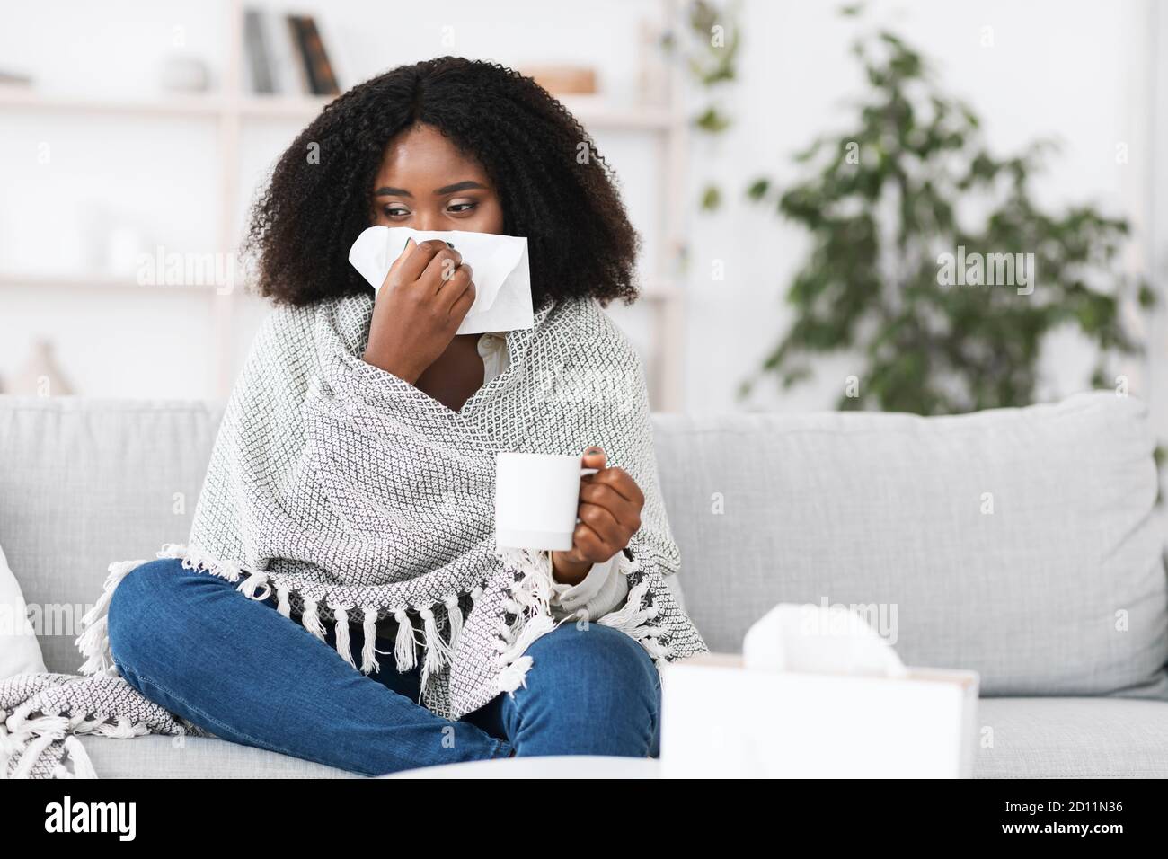 Malade afro femme enveloppée dans une couverture soufflant son nez de course Banque D'Images