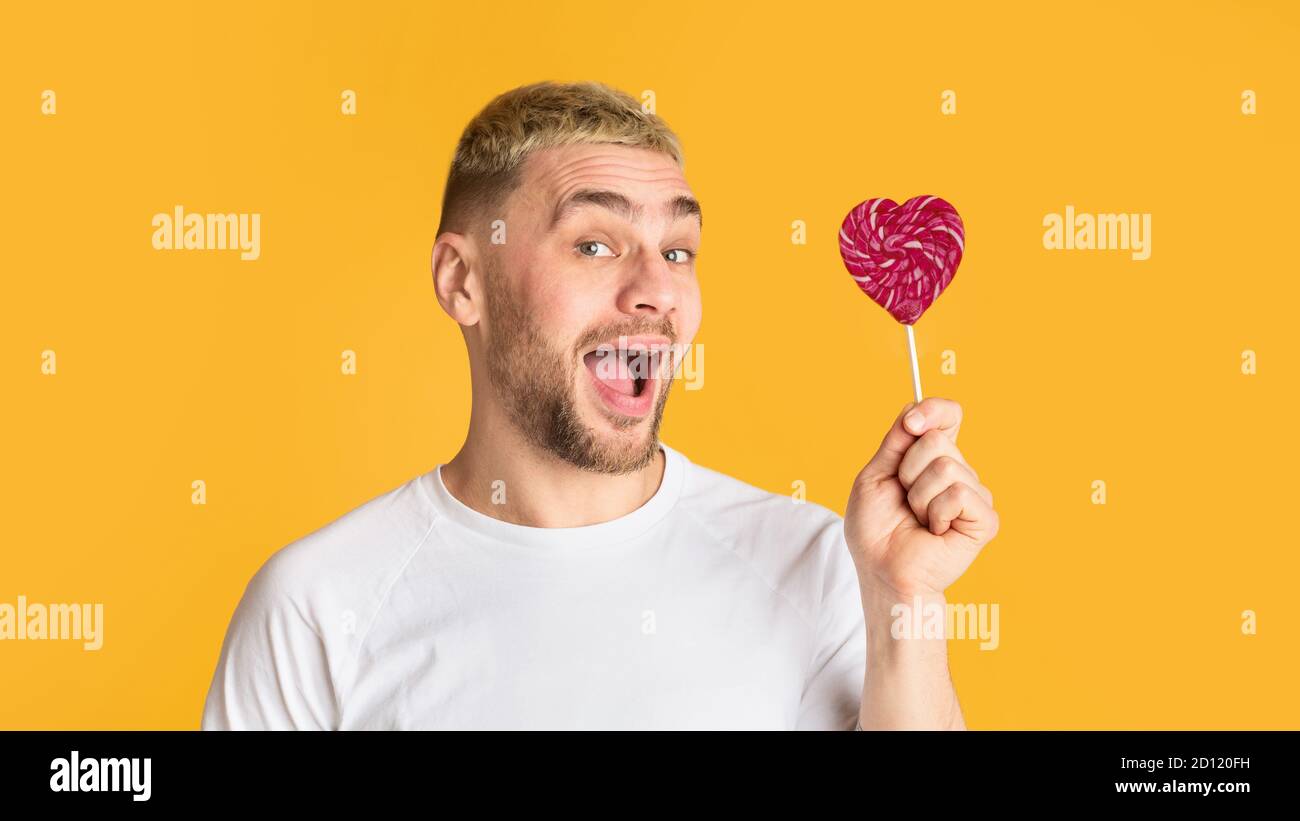 Homme émotionnel avec la bouche ouverte tient coeur lollipop Banque D'Images