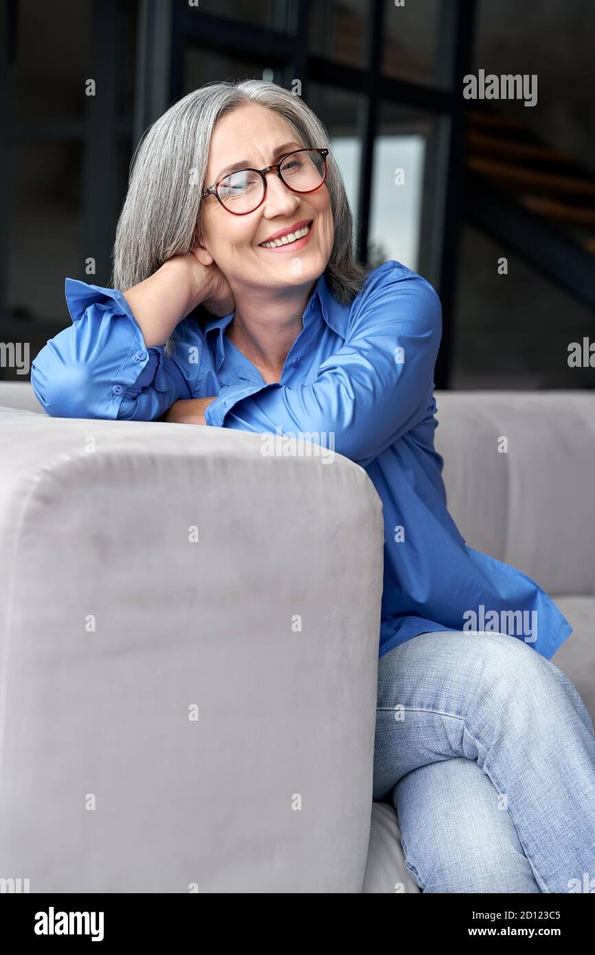 Heureuse détendue mature femme porte des lunettes assis sur le canapé à la maison, portrait. Banque D'Images