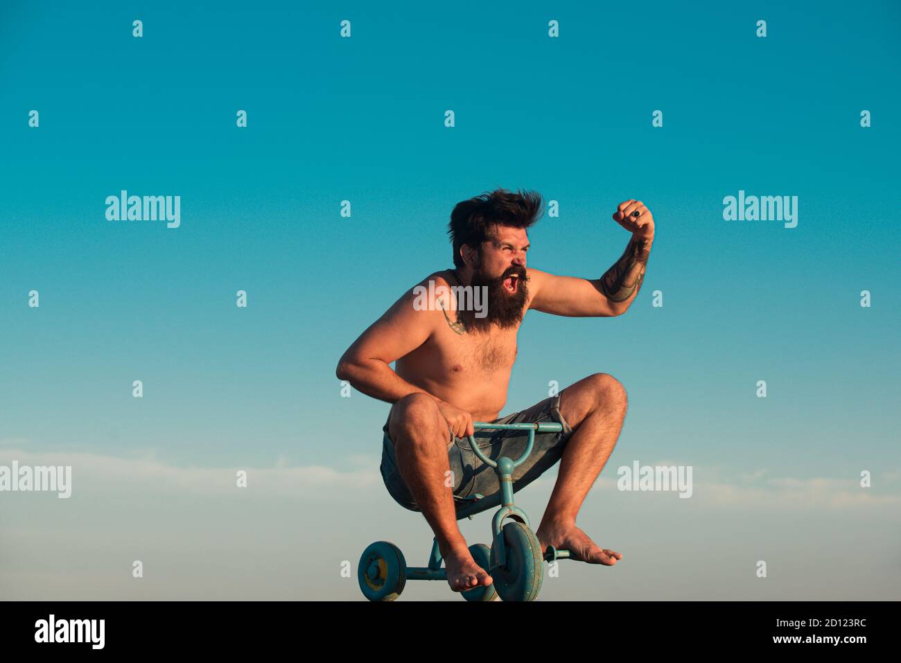 Guy tricycle d'équitation pour enfants. Portrait d'un homme barbu comme un hipster fou s'amusant avec le vélo dehors. Un jeune homme excités qui fait un petit vélo Banque D'Images