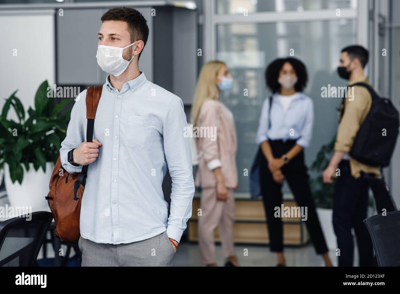 Distance sociale et travail au bureau après la quarantaine Covid-19. Focus sur homme millénaire avec masque de protection et sac à dos, regarde sur le côté dans le couloir Banque D'Images