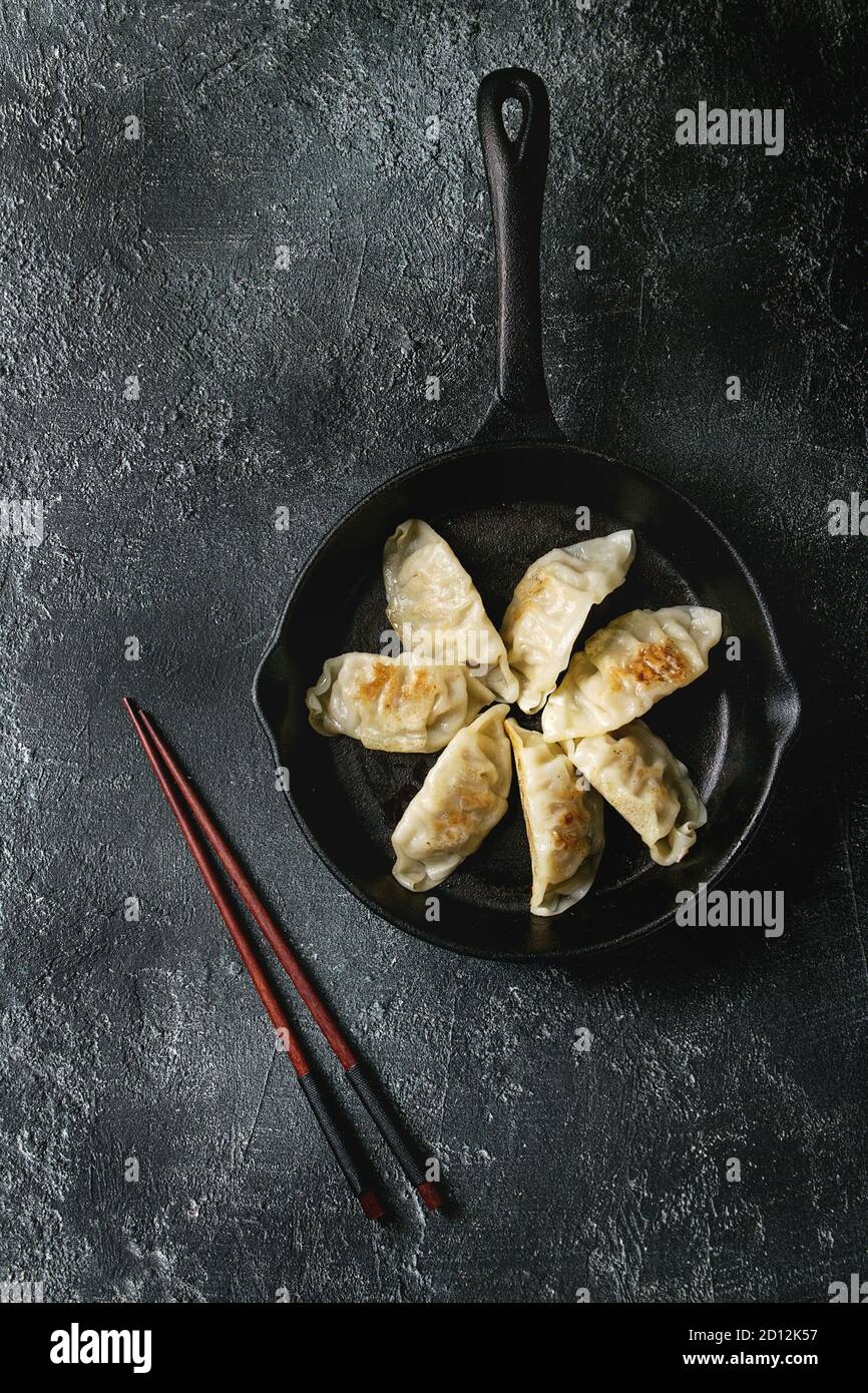 Les Gyozas raviolis frits potstickers asiatiques sur la fonte pan, servi avec des baguettes sur noir texture background. Vue de dessus, de l'espace. Banque D'Images
