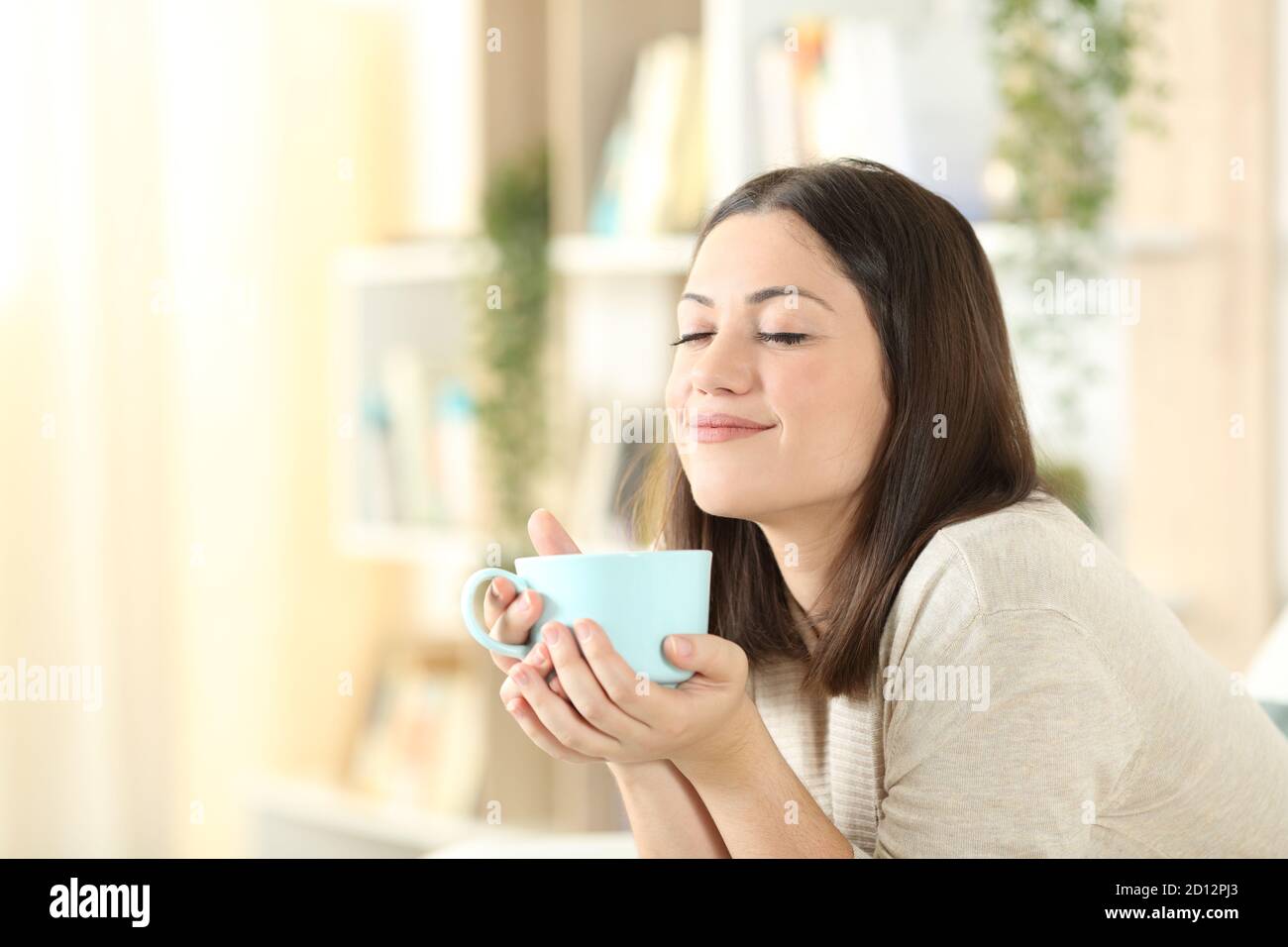 Femme satisfaite se détendant en tenant une tasse de café assis sur un canapé dans le salon à la maison Banque D'Images