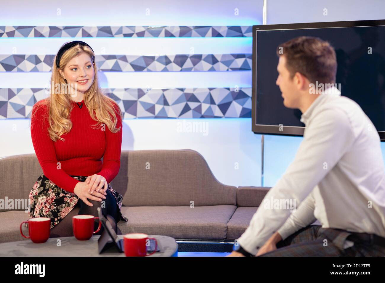 Deux animateurs de télévision parlent les uns avec les autres tout en étant assis sur un canapé dans un studio de cinéma, ils sont en train de filmer une émission de télévision. Banque D'Images