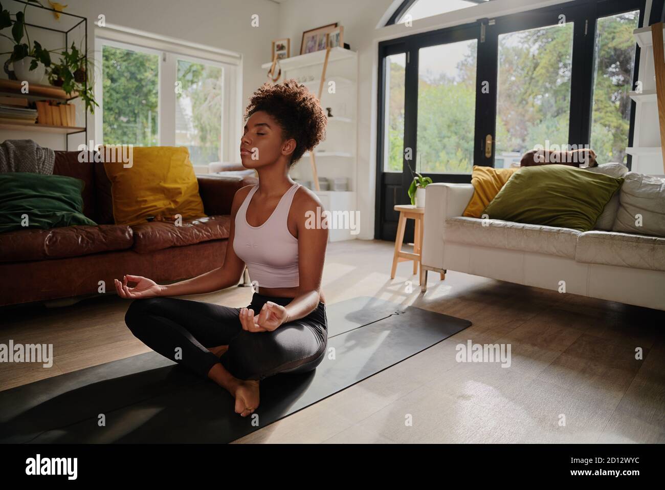 Jeune femme africaine méditant assise en position lotus à la maison sur le tapis de yoga Banque D'Images