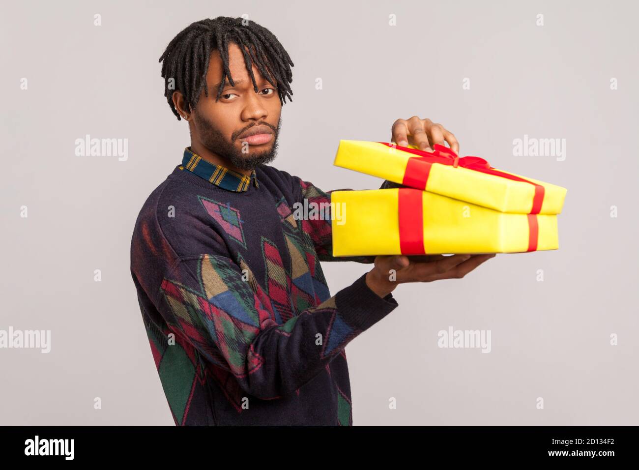 Mécontent homme africain déçu avec des dreadlocks tenant une boîte cadeau non emballé avec un visage frustré insatisfait, contrarié par le présent. Prise de vue en studio I Banque D'Images